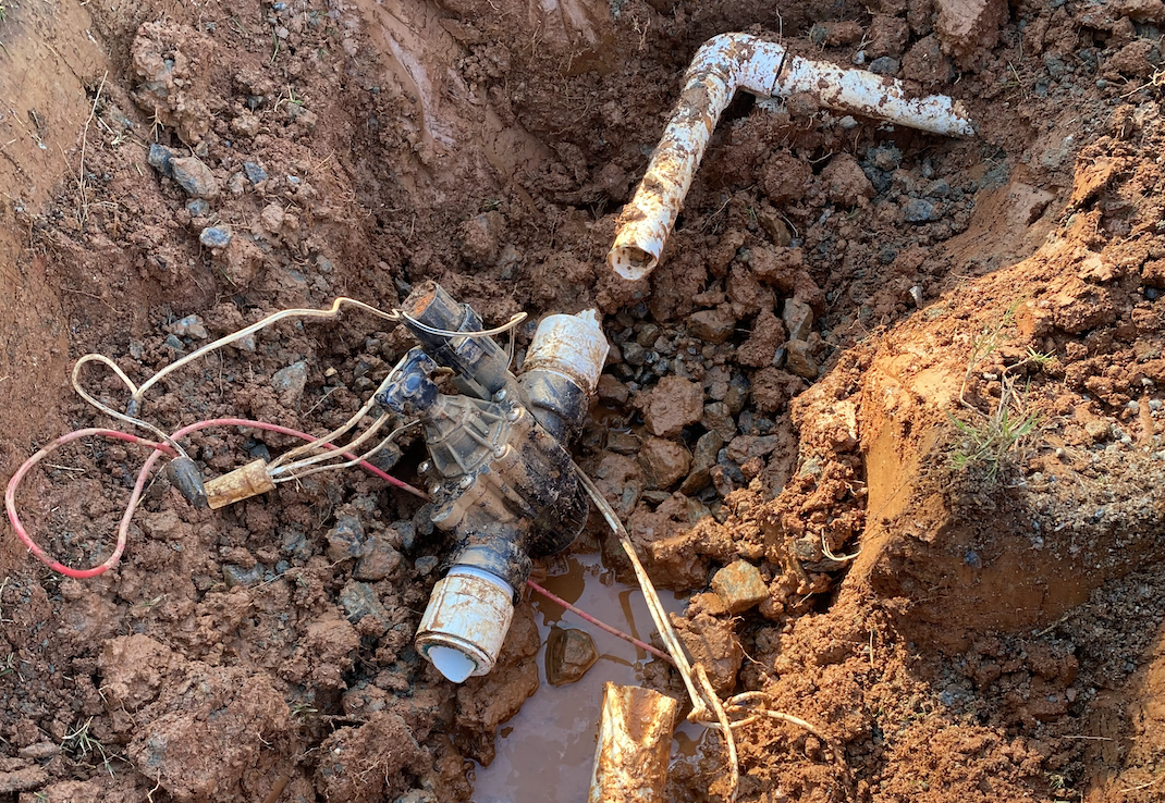 A pipe with attached wires lying in the dirt
