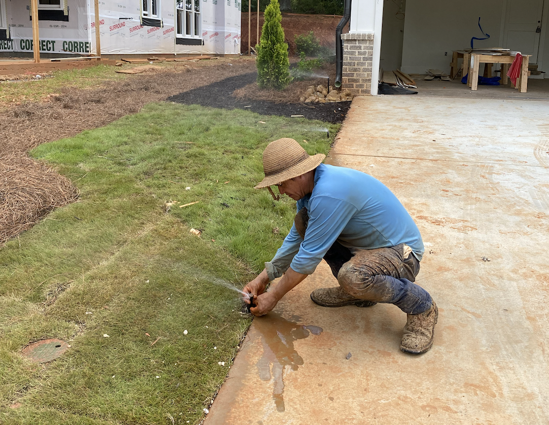 A man kneeling on the ground, watering a lawn with a hose