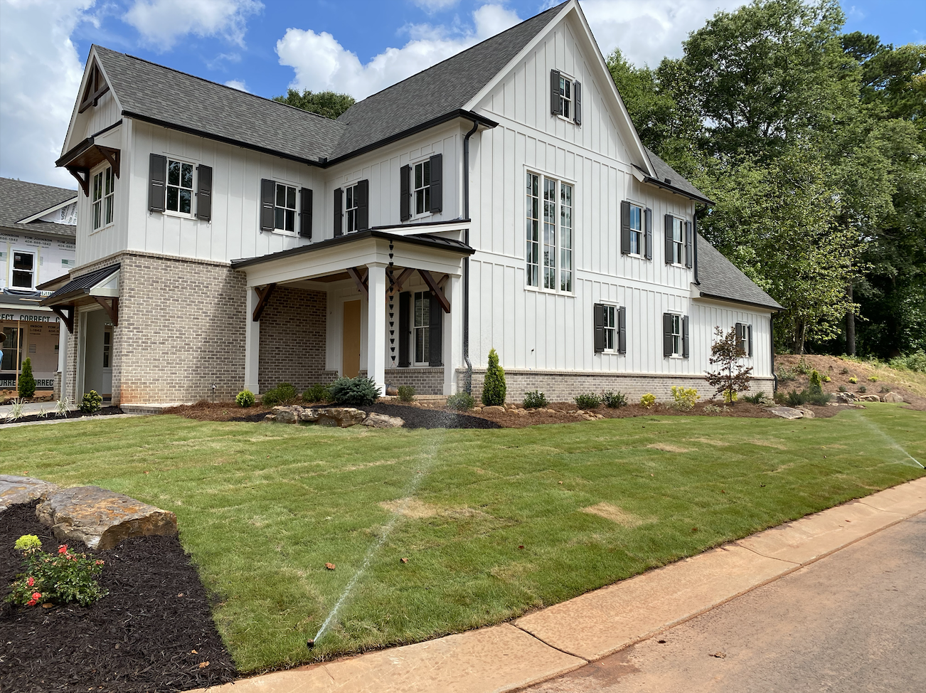 A spacious white house with a well-maintained lawn and beautiful landscaping surrounding it.